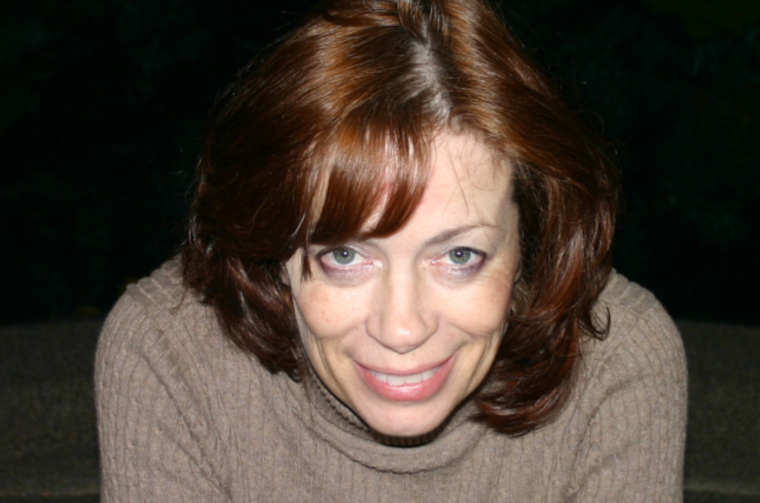 A profile image of a woman with red hair in a brown sweater